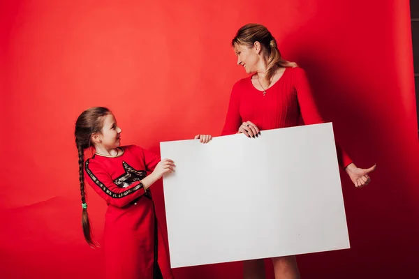 A girl and a mother holding a sign for an inscription on a red background — Stock Photo, Image