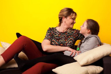 Anne ve kız, sarı arka planda, siyah bir kanepede.