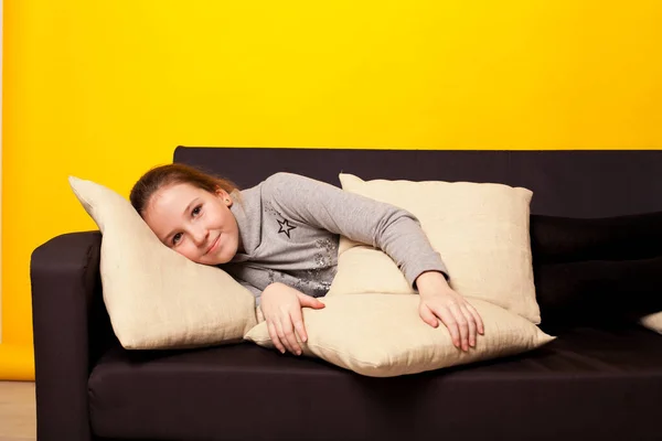 黄色の背景をした黒い家のソファの上の少女 — ストック写真