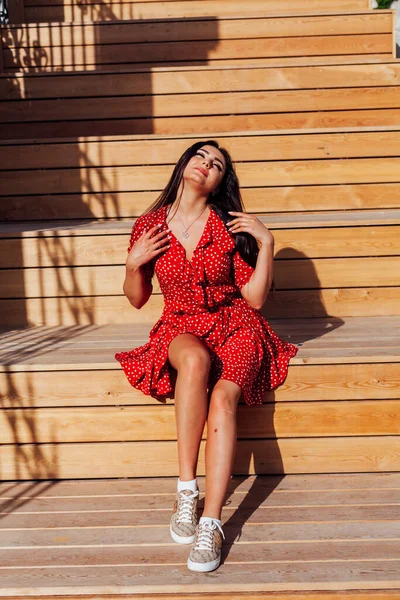Schöne brünette Frau in einem roten Sommerkleid geht die Straße hinunter — Stockfoto