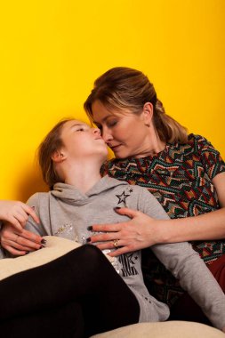 Anne ve kız, sarı arka planda, siyah bir kanepede.