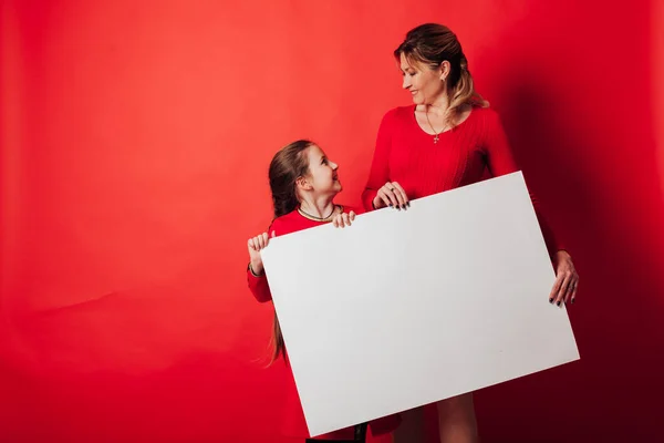 A girl and a mother holding a sign for an inscription on a red background — Stock Photo, Image