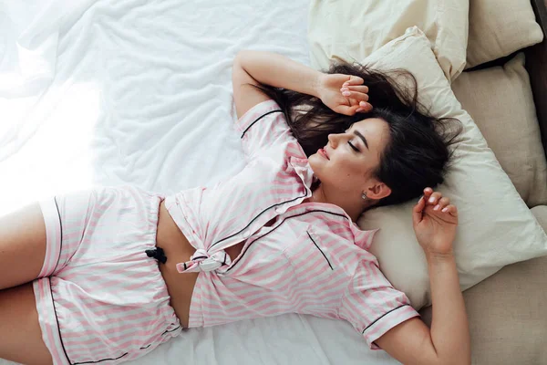 Gyönyörű nő rózsaszín pizsamában a hálószobában az ágyon — Stock Fotó