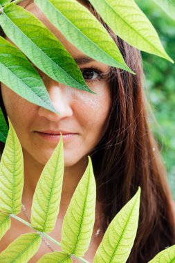 Yeşil yaprakların arasında bronzlaşmış güzel bir kadın.