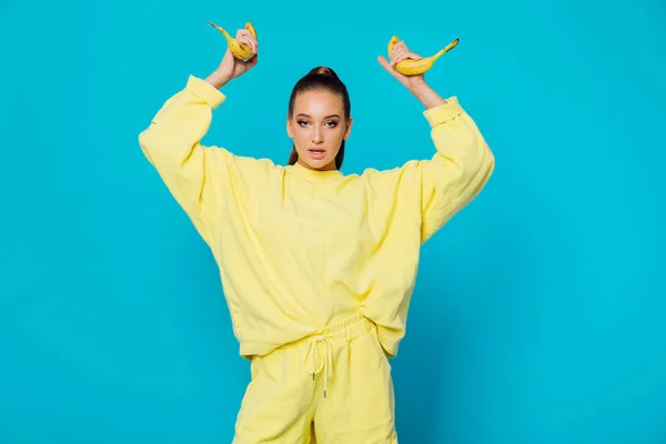 Mulher em roupas amarelas com frutas de banana em um fundo azul — Fotografia de Stock