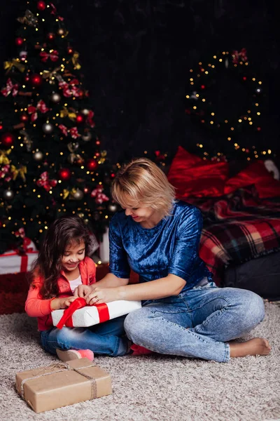 Маленькая кудрявая девочка и мама на елке с подарками новогодние огни гирлянды — стоковое фото