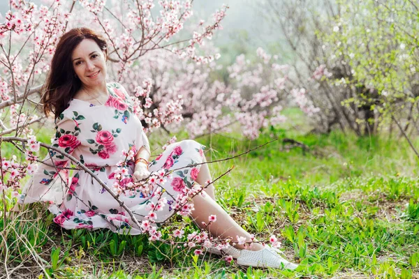 Bela mulher em um vestido de primavera em um jardim florescente com grama verde — Fotografia de Stock