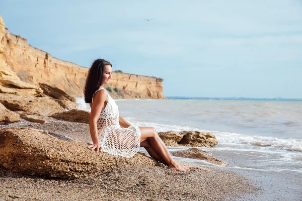 Deniz dalgalarının yanında kumlu bir sahilde oturan bir kadın