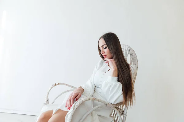 Una bella donna in un abito estivo leggero siede su una sedia bianca — Foto Stock