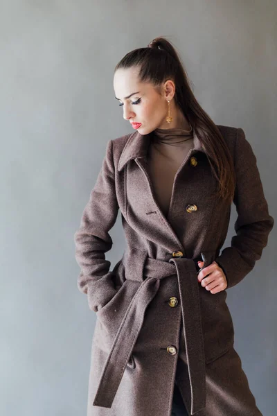 Женщина в теплом коричневом пальто на сером фоне — стоковое фото