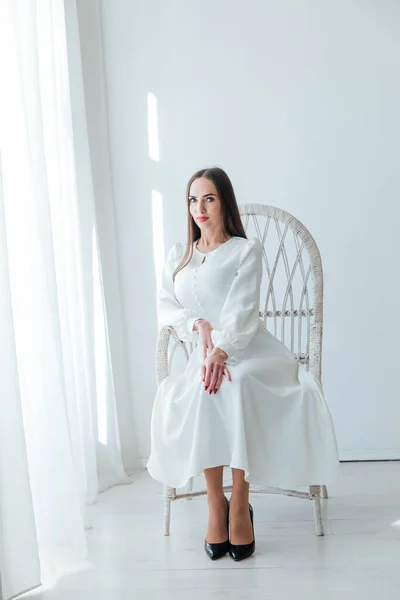 Beyaz elbiseli güzel bir kadın örgülü bir sandalyede oturuyor. — Stok fotoğraf