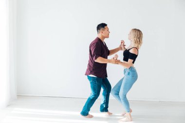 Bir kadın ve bir adam beyaz bir salonda Bachata 'nın müziğiyle dans ediyorlar.