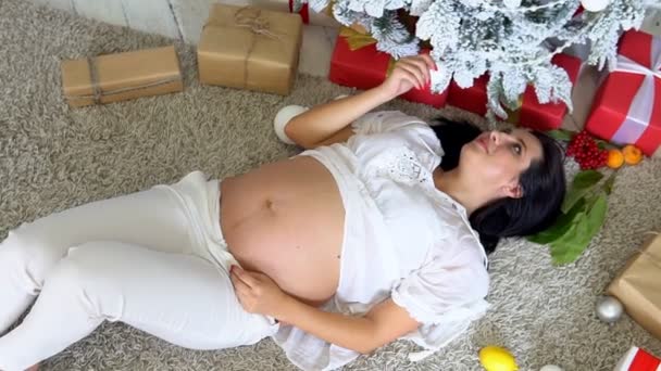 Gyönyörű terhes nő fekszik a karácsonyfa új év — Stock videók
