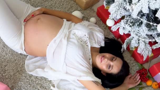 Krásná těhotná žena leží u vánočního stromečku nový rok — Stock video