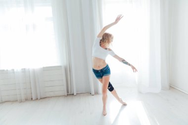 Güzel, ince bir kadın beyaz bir salonda müzikle dans ediyor.