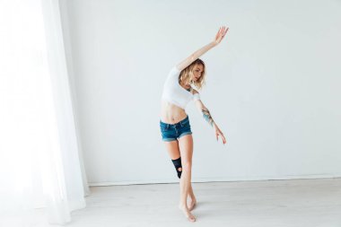 Güzel, ince bir kadın beyaz bir salonda müzikle dans ediyor.