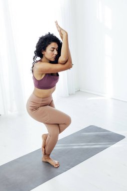 Beyaz salonda yoga yapan esmer kadın jimnastik yapıyor.