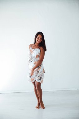 Beyaz bir odada, yaz elbisesi içinde bronzlaşmış güzel bir kadın.