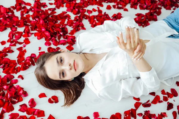 Piękna kobieta leży w kwiatach płatków czerwonych róż — Zdjęcie stockowe