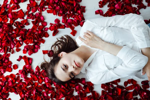 Une belle femme gît dans les fleurs des pétales de roses rouges — Photo
