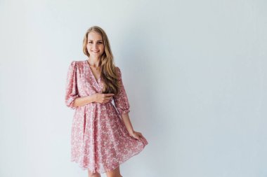 Beyaz bir odada, yazlık elbiseli güzel sarışın kadın.