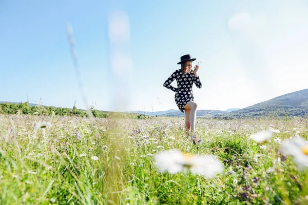Una hermosa mujer camina en un campo con flores de manzanilla — Foto de Stock