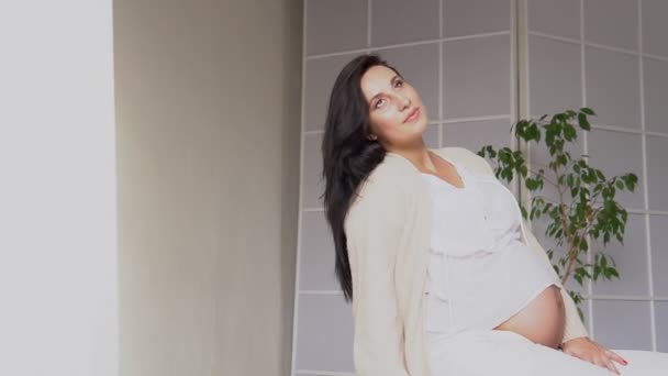 Όμορφη έγκυος γυναίκα στο σπίτι σε ένα λευκό δωμάτιο περιμένει για ένα μωρό — Αρχείο Βίντεο