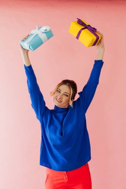 40 yaşında bir kadın pembe arka planda hediyeler tutuyor.