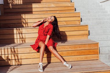 Yazlık kırmızı elbiseli güzel esmer kadın dışarıda yürüyor.