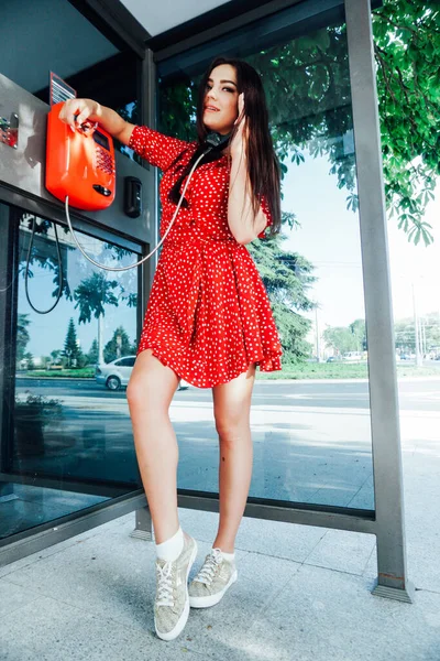 Schöne brünette Frau in rotem Kleid spricht Payphone — Stockfoto