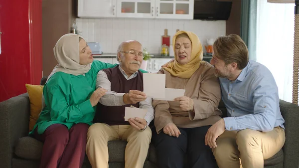 A Muslim Turkish family looking at old photos in their living room. The old father with his children and his hijab wife are happy looking at old photos.