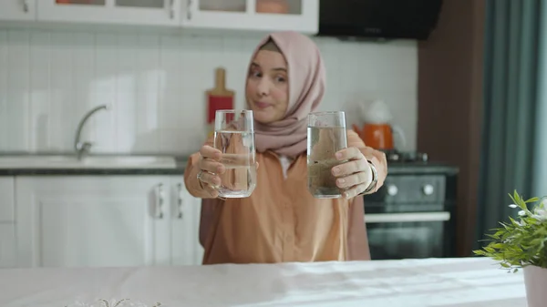 Muslim hijab dressed woman in hijab holding a dirty glass in one hand and a clean glass in the other. The woman is disturbed by the pollution of the water and draws attention to this problem.