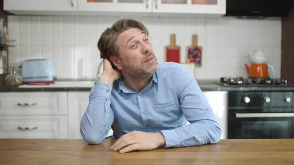 Unhappy depressed man. Stressed from work, worried, heartbroken. Thinking young man sitting alone in the kitchen.