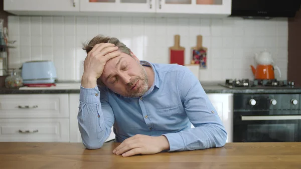 Unhappy depressed man. Stressed from work, worried, heartbroken. Thinking young man sitting alone in the kitchen.