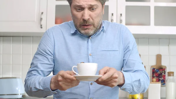 The man drinking coffee at home spills his coffee. Portrait of man preparing himself coffee to drink. The man who spills his coffee gets upset.