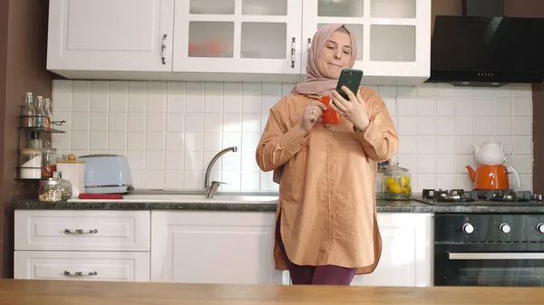 Νεαρή Γυναίκα Μαντίλα Κρατώντας Smartphone Ακουμπά Στον Πάγκο Της Κουζίνας — Φωτογραφία Αρχείου