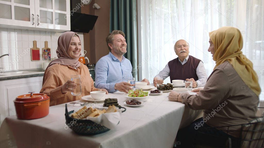 Happy Muslim family having iftar dinner together in the kitchen. A Muslim Turkish family breaks their fast at the iftar table. Iftar is the evening meal at which Muslims 