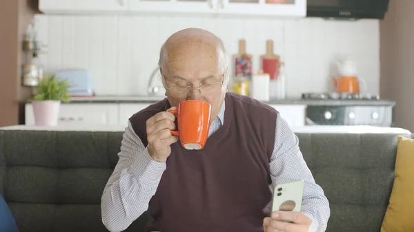 Старик Смотрит Смешное Видео Своем Смартфоне Пьет Кофе Дома Мужчина — стоковое фото