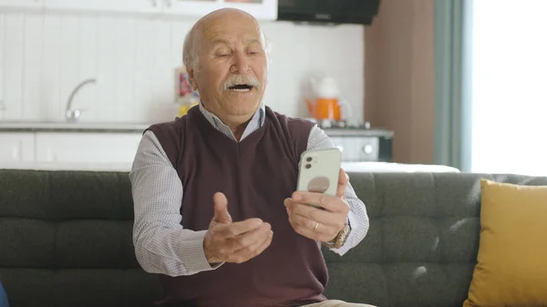 The old man dials the number on the smartphone. Old man sends sms to mobile phone while home. 80s old man looking at mobile apps, sms and news on his smartphone.