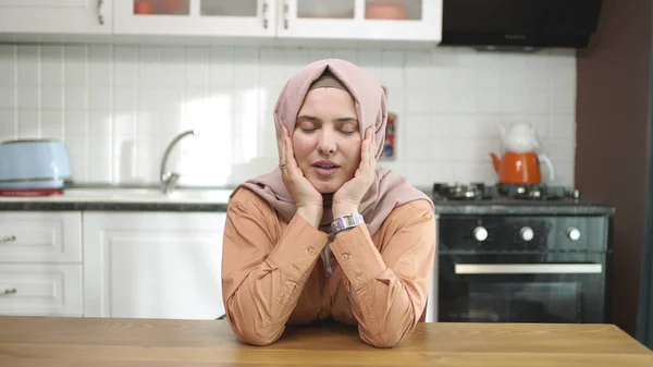 Unhappy depressed woman. Stressed from work, worried, heartbroken. Young woman wearing hijab thinking head in hands sitting alone in kitchen at home.