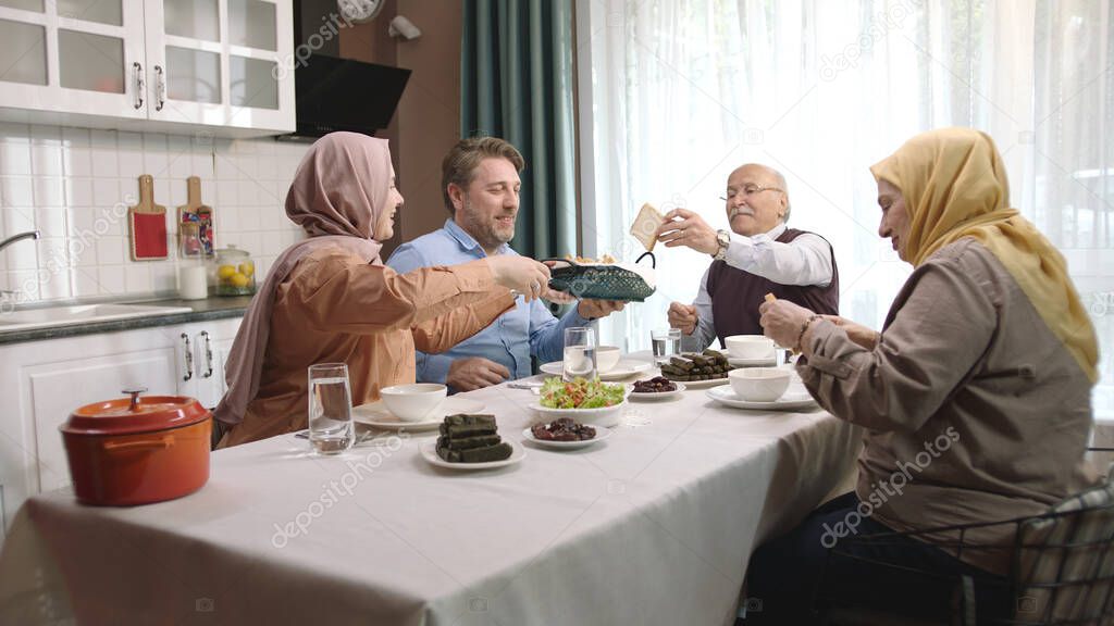 Happy Muslim family having iftar dinner together in the kitchen. A Muslim Turkish family breaks their fast at the iftar table. Iftar is the evening meal at which Muslims 