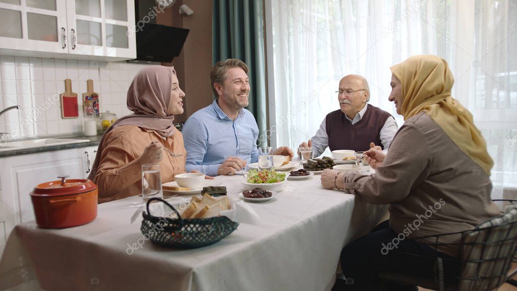 Happy Muslim family having iftar dinner together in the kitchen. A Muslim Turkish family breaks their fast at the iftar table. Iftar is the evening meal at which Muslims 