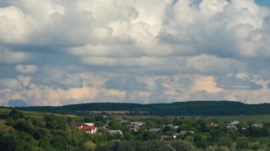 Kırsal alandaki küçük evlerin üzerinde mavi gökyüzünde hızla ilerleyen beyaz kabarık kümülüs bulutlarının hızlandırılmış görüntüleri.