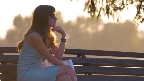 暖かい夏の夜を楽しむ湖側のベンチに座っている孤独な女性 孤独とリラクゼーションの概念 — ストック動画