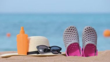 Hasır şapka, takunya ayakkabılar, güneş kremi ve sıcak güneşli bir günde tropikal sahilde kumlu plajda siyah koruyucu güneş gözlüğü. Yaz tatili kavramı.