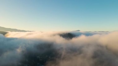 Gün batımında dağ tepelerini ve köy evlerini kaplayan karamsar sis bulutlarının hava manzarası.