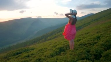 Kırmızılı genç kadın çimenli bir tarlada duruyor rüzgarlı bir sonbahar akşamında doğanın tadını çıkarıyor..