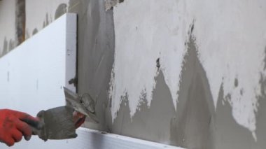 İnşaat işçisi ev duvarını yapışkan çimento yapıştırıcısıyla kaplıyor berore termal koruma için köpük yalıtım çarşafları yerleştiriyor..