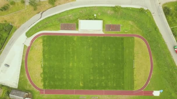 Luftaufnahme des Sportstadions mit roten Laufbahnen und grünem Rasen Fußballplatz in der Nähe von Schulgebäuden im ländlichen Raum. — Stockvideo