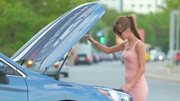 Motorista feminina que abre o capô do carro inspecionando o motor quebrado em uma rua da cidade. Conceito de anomalia do veículo. — Vídeo de Stock